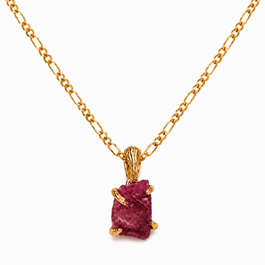 A gold chain necklace with a pendant featuring a rough, rectangular pinkish-red gemstone in a textured gold setting, shown against a plain white background.