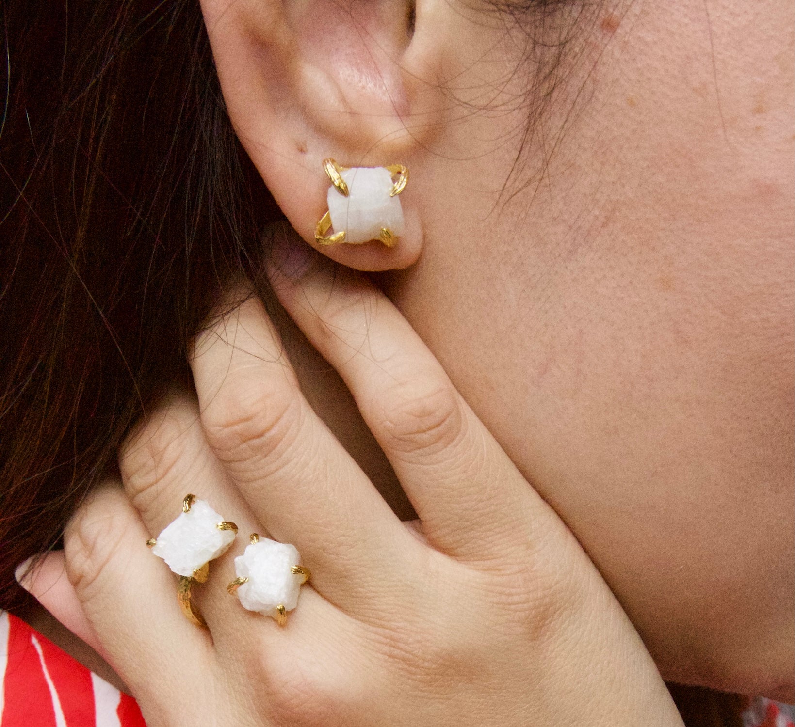 A close-up lifestyle shot of a person wearing  Elemental Rose Moonstone gemstone jewellery by WJY studio matching white and gold jewelry, featuring a pair of stud earrings and matching ring clips on their fingers.